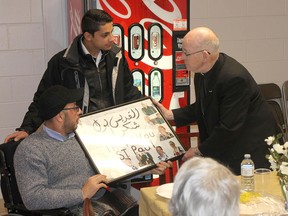 Mahmoud Maree, seated, and his son Mohammad make a presentation to Father Leo Byrne during a thank you dinner from the family of six on Saturday to their sponsorship group from Kingston's St. Paul the Apostle Church. (Supplied photo)