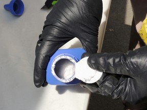 In this file photo provided by the Royal Canadian Mounted Police, a member of the RCMP opens a printer ink bottle containing the opioid carfentanil imported from China, in Vancouver. Drug dealers have been cutting carfentanil and its weaker cousin, fentanyl, into heroin and other illicit drugs to boost profit margins. Royal Canadian Mounted Police photo