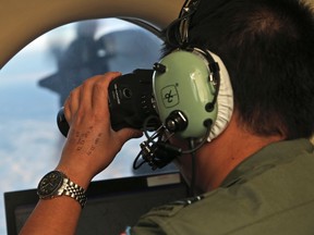 In this March 22, 2014, file photo, flight officer Jack Chen uses binoculars at an observers window on a Royal Australian Air Force P-3 Orion during the search for missing Malaysia Airlines Flight MH370 in Southern Indian Ocean, Australia. The Joint Agency Coordination Center in Australia said Tuesday, Jan. 17, 2017, that the search for Malaysia Airlines Flight 370 had officially been suspended after crews finished their fruitless sweep of the 120,000-square kilometre (46,000-square mile) search zone west of Australia. (AP Photo/Rob Griffith, File)
