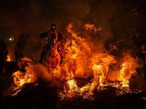 A man rides a horse through a bonfire as part of a ritual in honor of Saint Anthony the Abbot, the patron saint of domestic animals, in San Bartolome de Pinares, west of Madrid, Spain on Monday, Jan. 16, 2017. On the eve of Saint Anthony's Day, hundreds ride their horses through the narrow cobblestone streets of the small village of San Bartolome during the "Luminarias," a tradition that dates back 500 years and is meant to purify the animals with the smoke of the bonfires and protect them for the year to come. (AP Photo/Daniel Ochoa de Olza)