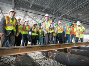 Ontario Transport Minister Bob Chiarelli (L), Mayor Jim Watson take turns hammering a spike while others look on  during a ceremony marking the laying of the first official rail track of the O-Train Confederation Line light rail transit project at the Belfast Yard maintenance and storage facility on June 12, 2015.