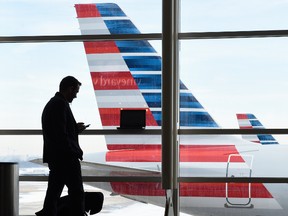 In this Jan. 25, 2016, file photo, a passenger talks on the phone as American Airlines jets sit parked at their gates at Washington's Ronald Reagan National Airport. American Airlines announced Wednesday, Jan. 18, 2017, that passengers will be able to buy “basic economy” tickets starting in February that will be similar to bare-bones fares already offered by Delta Air Lines and soon to be matched by United Airlines. The basic-economy fares will have a lower price, but will offer fewer comforts. (AP Photo/Susan Walsh, File)