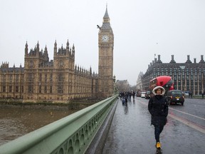 A woman walks across Westminster Bridge past the Houses of Parliament during a snow flurry in London on January 13, 2017.  ISABEL INFANTES/AFP/Getty Images