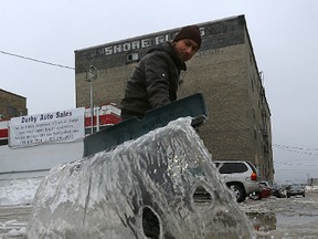 Waqas Hashmi takes a shovel to a puddle in an attempt to prevent the entrance to Derby Auto Sales on Derby Street at Jarvis Avenue in Winnipeg from freezing up later in the day on Sunsay, Jan. 22, 2017. (Kevin King/Winnipeg Sun/Postmedia Network)