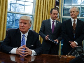 National Trade Council adviser Peter Navarro, right, and White House Chief of Staff Reince Priebus, centre, await U.S. President Donald Trump's signing three executive orders in the Oval Office of the White House in Washington on Monday, Jan. 23, 2017. (AP Photo/Evan Vucci)