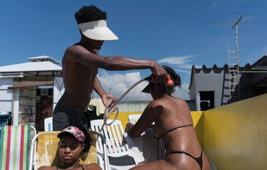 In this Jan. 15, 2017 photo, an employee sprays a customer wearing a bikini made out of black electrical tape, in order to attain crisp tan lines, at the rooftop Erika Bronze salon in the suburb of Realengo in Rio de Janeiro, Brazil. Despite being sprinkled with water, some tanners feel dizzy or even faint after a rooftop session. (AP Photo/Renata Brito)