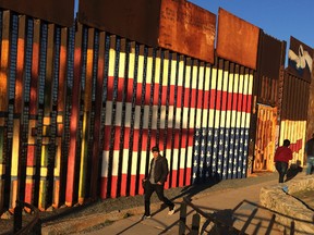 People pass graffiti along the border structure in Tijuana, Mexico, on Wednesday, Jan. 25, 2017. (AP Photo/Julie Watson)