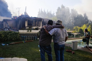 Two men comfort each other as they watch the remains of a house burn in Concepcion, Chile, Thursday, Jan. 26, 2017. The worst forest fires in Chile's history were uncontrolled on Wednesday, killing multiple emergency personnel caught in the flames as they tried to help families in rural communities, authorities said. (Alejandro Zonez/Aton via AP)