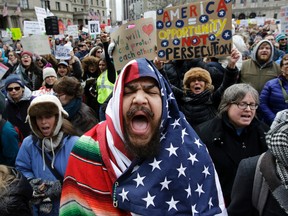 Izzy Berdan, of Boston, center, wears an American flags as he chants slogans with other demonstrators during a rally against President Donald Trump's order that restricts travel to the U.S., Sunday, Jan. 29, 2017, in Boston. Trump signed an executive order Friday, Jan. 27, 2017 that bans legal U.S. residents and visa-holders from seven Muslim-majority nations from entering the U.S. for 90 days and puts an indefinite hold on a program resettling Syrian refugees. (AP Photo/Steven Senne)