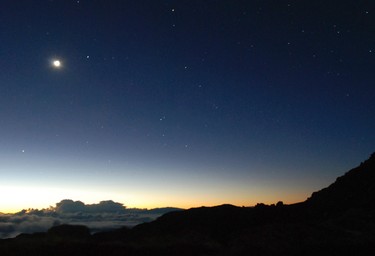 The moon hangs above the horizon as the glow of the sun begins to fill the sky in front of the summit of Haleakala volcano in Haleakala National Park on Hawaii's island of Maui, Tuesday, Jan. 24, 2017. Park officials say the sunrise on Haleakala attracts over a thousand people a day, resulting in an overload of visitors and creating a safety hazard. As a result, anyone wanting to see the sunrise on the summit will now be required to make reservations in advance and pay a small fee. (AP Photo/Caleb Jones)