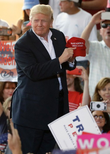 U.S. President Donald Trump points to a slogan on a hat during the "Make America Great Again Rally" at Orlando-Melbourne International Airport Saturday, Feb. 18, 2017, in Melbourne, Fla. (AP Photo/Chris O'Meara)