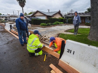 In this Friday, Feb. 17, 2017, photo Duarte city employees install wood barrier between the K-Rails on Melcanyon Road in Duarte, Calif., as homeowners view the progress only hours before the arrival of a major storm.   (Walt Mancini/Los Angeles Daily News via AP)