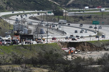 Traffic passes along the scene , Saturday, Feb., 18, 2017, where a tractor trailer and a San Bernardino County Fire Department fire engine fell on Friday from southbound Interstate 15 where part of the freeway collapsed due to heavy rain in the Cajon Pass, Calif., Saturday, Feb. 18, 2017. (David Pardo/The Daily Press via AP)