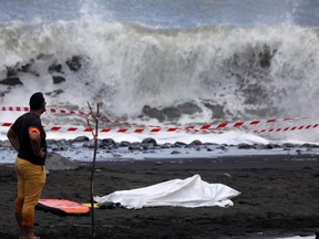 A policeman stands next to the body of a bodyboarder killed by a shark, covered by a white cloth next to his bodyboard, on February 21, 2017 on a beach in Saint-Andre, on the French Reunion Island in the Indian Ocean. (RICHARD BOUHET/AFP/Getty Images)