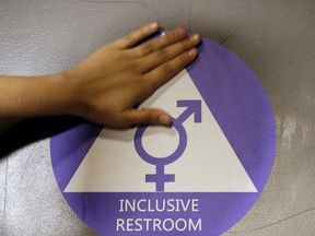 A new sticker is placed on the door at the ceremonial opening of a gender neutral bathroom at Nathan Hale High School in Seattle on May 17, 2016. A government official says the Trump administration will revoke guidelines that say transgender students should be allowed to use bathrooms and locker rooms matching their chosen gender identity. (Elaine Thompson/AP Photo/File)
