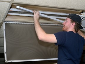 Michael Urquhart of G+S Electric installs an LED light tube in a classroom at St. Thomas Aquinas secondary school Monday. (MORRIS LAMONT, The London Free Press)