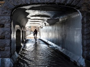 A cyclist makes his way through some standing water along the Queen Elizabeth Driveway underneath the Pretoria Bridge in Ottawa on a mild winter day March 8, 2017.