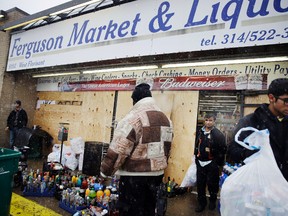 In this Wednesday, Nov. 26, 2014, file photo, Kush Patel, right, carries out bags of merchandise while helping his uncle Andy Patel, rear, clean up the looting damage from Monday’s riots at his store in Ferguson, Mo. (AP Photo/David Goldman, File)