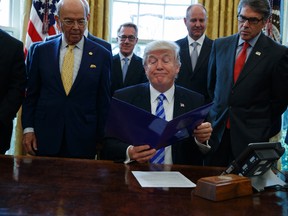 President Donald Trump, flanked by Commerce Secretary Wilbur Ross, left, and Energy Secretary Rick Perry, is seen in the Oval Office of the White House in Washington, Friday, March 24, 2107, where he announced the approval of a permit to build the Keystone XL pipeline, clearing the way for the $8 billion project. (AP Photo/Evan Vucci)