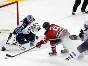 Devils forward Taylor Hall tries to get a shot way on Jets goalie Connor Hellebuyck as Blake Wheeler defends during overtime in Newark, N.J. last night. (AP)