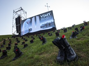 Military boots and poppies lay around the Canadian National Vimy Memorial as a screen displays a graphic ahead of a Sunset Ceremony on April 8, 2017 in Vimy, France. (Photo by Jack Taylor/Getty Images)