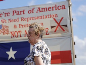 In this Thursday, Sept. 17, 2015, photo, Pamela Taylor, whose home is on the south side of the border fence, stands near a sign she erected, in Brownsville, Texas. (AP Photo/Eric Gay, File)