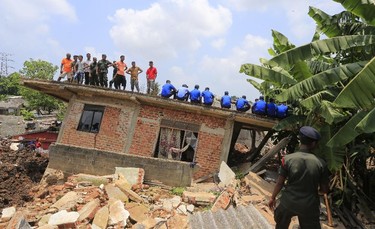 Sri Lankan military rescuers and onlookers rest on top of a damaged house at the site of a garbage dump collapse in Meetotamulla, on the outskirts of Colombo, Sri Lanka, Sunday, April 16, 2017. The death toll from the collapse of the massive garbage mound near Sri Lanka's capital rose to more than a dozen Sunday, and residents feared more victims could be buried underneath the debris. Maj. Gen. Sudantha Ranasinghe, who is heading the rescue efforts, said 78 houses were destroyed and more than 150 were damaged. (AP Photo/Eranga Jayawardena)