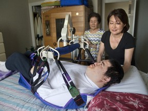 Alex Cha, 48, is lowered to his bed by his mom, Jeong Cha, 78, and guided by his sister, Jin Cha, at their north London condominium on Tuesday, April 11, 2017. (MIKE HENSEN, The London Free Press)