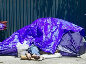 A homeless person sleeps beneath a tarp covering a tent. FREDERIC J. BROWN/AFP/Getty Images