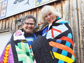 Denise Corneil, left, and Mary Simpson stand outside Corneil's house in Wardsville Ontario. They're draped in a collage of barn quilts, designs they picked out for a little project to commemorate Wardsville's bicentennial in 2010.