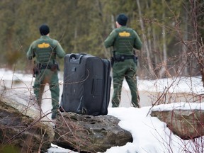 An abandoned suitcase sits on the United States side of the border with Canada left there by an asylum seeker as U.S. border patrol guards pass by, Tuesday, March 28, 2017 near Hemmingford, Que. (THE CANADIAN PRESS/Paul Chiasson)