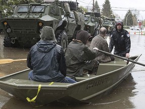 Montreal police officer helps residents of flooded avenue du Chateaux-Pierrefonds as they make their way past Canadian military personnel TAPV, on the in Montreal on Sunday May 7, 2017. (Pierre Obendrauf/POSTMEDIA)