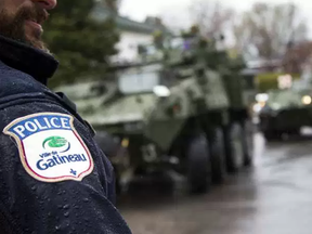 The Canadian Forces were called into Gatineau to help with the flooding in Gatineau Sunday May 7, 2017. A Gatineau Police officer stands along Rue Notre Dame as military vehicles pull in. Ashley Fraser/Postmedia