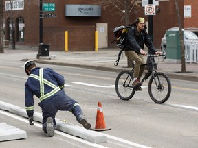 A cyclist passes as workers with Concrete Inc., install lanes for the permanent downtown bike lane system along 100 Avenue near 104 Street in Edmonton. (FILE)