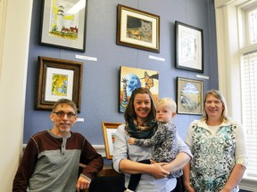 David Doyle (left), Sarah Verhoog with daughter Lorelei, and Deb Elligsen of the Mitchell & Area Arts Group stand in front of a wall at the West Perth library which has some of their art on display for the public. ANDY BADER/MITCHELL ADVOCATE