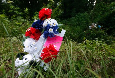 A small flowered tribute with a personalized note to Kingston Frazier, a six-year-old boy who was found shot dead Thursday, in his mother's stolen car along a no-outlet road in Gluckstadt, Miss., rests by an area where the vehicle was allegedly removed, Friday, May 19, 2018. Three individuals have been arrested for the death and will have an initial appearance before a judge Monday. (AP Photo/Rogelio V. Solis)
