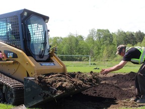 Justin Erickson, right, works with Dave Steer, driving the front-end loader, at the soccer field behind the Stoneybrook Baptist Church. The men spent the day repairing the northeast London pitch after vandals drove an SUV over it. (DALE CARRUTHERS, The London Free Press)
