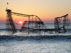 In this Feb. 25, 2013, file photo, the sun rises behind the Jet Star roller coaster, partially submerged in the Atlantic Ocean after Superstorm Sandy destroyed part of the Casino Pier in Seaside Heights, N.J. A new roller coaster named Hydrus, built safely inland above the beach rather than out over the water, opened May 6, 2017, more than four years after the storm caused billions of dollars' worth of damage to the coast. (AP Photo/Mel Evans, File)
