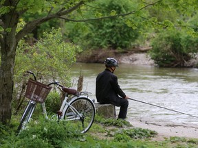 A cyclist fishes for carp in Gibbons Park. A London MP is trying get the Thames River included in the Navigation Protection Act. (MIKE HENSEN, The London Free Press)
