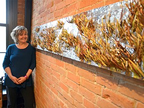 Local artist Jane Derby stands in front of pieces from her new exhibit Gouging, Nailing, Cutting, Scraping & Painting, which debuted Tuesday at Studio 22. (Megan Glover/For The Whig-Standard)
