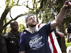 In an April 29, 2017 photo provided by John Rudoff, Jeremy Joseph Christian is seen with an American flag draped over his back during a Patriot Prayer organized by a pro-Trump group in Portland, Ore. Christian, who police say fatally stabbed two other men who tried to shield young women from an anti-Muslim tirade on a Portland light-rail train Friday, made his first court appearance in Portland on Tuesday. (John Rudoff via AP)