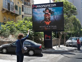 A woman waves for taxi, as she stands in front of a digital billboard promoting the 2017 Wonder Woman movie, in Beirut, Lebanon, Tuesday, May 30, 2017. Lebanon's ministry of economy says it has asked the country's security agency to ban the movie because its lead actress, Gal Gadot, is an Israeli. (AP Photo/Hussein Malla)