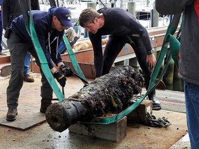 In this May 24, 2017 photograph provided by the U.S. Navy, Naval History and Heritage Command underwater archaeologist George Schwarz, right, and Explosive Ordnance Disposal Technician Senior Chief Mark Faloon, left, stand over and prepare a cannon for transportation at Dodson Boat Yard in Stonington, Conn. to the Washington Navy Yard. The cannon is believed to be from the wreck of U.S.S. Revenge in 1811. (NHHC underwater archaeologist Heather G. Brown/U.S. Navy via AP)