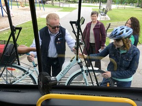 Kingston Transit bus operator Paul Lollar helps Lisa Stanulis lift her bike off a rack on the front of a bus at the kickoff to this week’s Commuter Challenge in City Park on Monday. (Elliot Ferguson/The Whig-Standard)