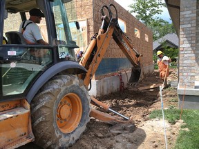 London Hydro employees Dennis Willert, in the excavator and Troy Haggitt, finish off filling up a trench after they hauled electrical cables (along with Bell and Rogers cables) from the street to a new home under construction in northwest London. Photograph taken on Tuesday May 30, 2017. (MIKE HENSEN, The London Free Press)