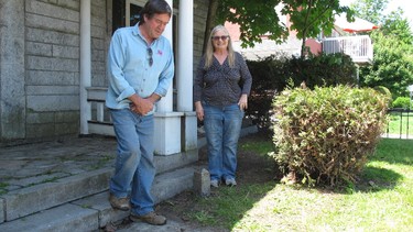 In this photo taken on June 8, 2017 in Derby, Vt., Brian and Joan Dumoulin pose on both sides of a marker showing the U.S.-Canadian border in the front yard of their home. She is in Canada, while he is in the United States. Straddling the border between the Derby neighbourhood of Beebe Plain, Vt., and Stanstead, Que., has made their house more difficult to sell. (AP Photo/Wilson Ring)