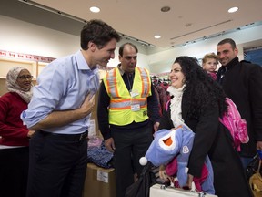 Prime Minister Justin Trudeau gives newly-arrived Syrian refugee Sylvie Garabedian, centre, a winter jacket at Pearson International airport on Dec. 11, 2015. (THE CANADIAN PRESS)