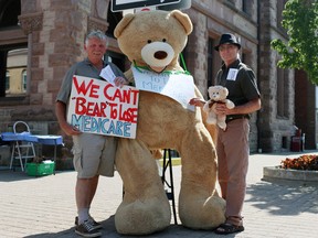 Ontario Health Coalition volunteer Peter Boyle and Oxford Social Justice Coalition chair Bryan Smith (from left to right) stand with a seven-foot-tall teddy bear to spread the message that 'We Can't Bear to Lose Medicare' on Sunday in front of city hall.