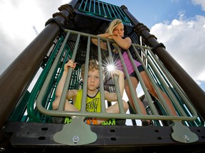 Zander van Schaik, left, 6, and his sister Mackenzie van Schaik, 10, peer through metal bars that have been installed where a slide once existed on the playground adjacent to the Westridge Wolf Willow Country Club Community League Hall in west Edmonton on June 15, 2017. Three slides from the playground were removed after the American company that sells them issued a recall.