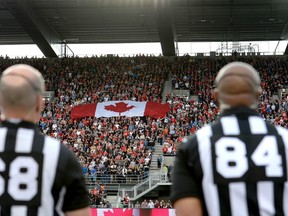 Officials look on as a Canada flag is held up by fans during the national anthem O Canada before the Ottawa Redblacks season opener against the Calgary Stampeders in Ottawa on June 23, 2017. (Justin Tang/The Canadian Press)